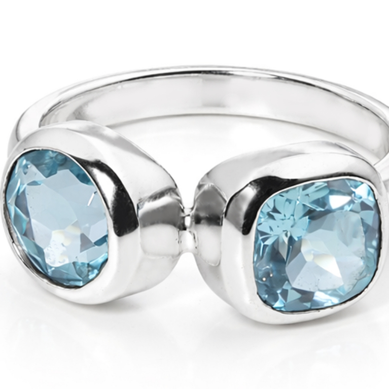 Handmade sterling silver open ring featuring two genuine cushion cut sky blue topaz gemstones in polished bezel settings with an ultra mirror polished 925 sterling silver band on a white background.